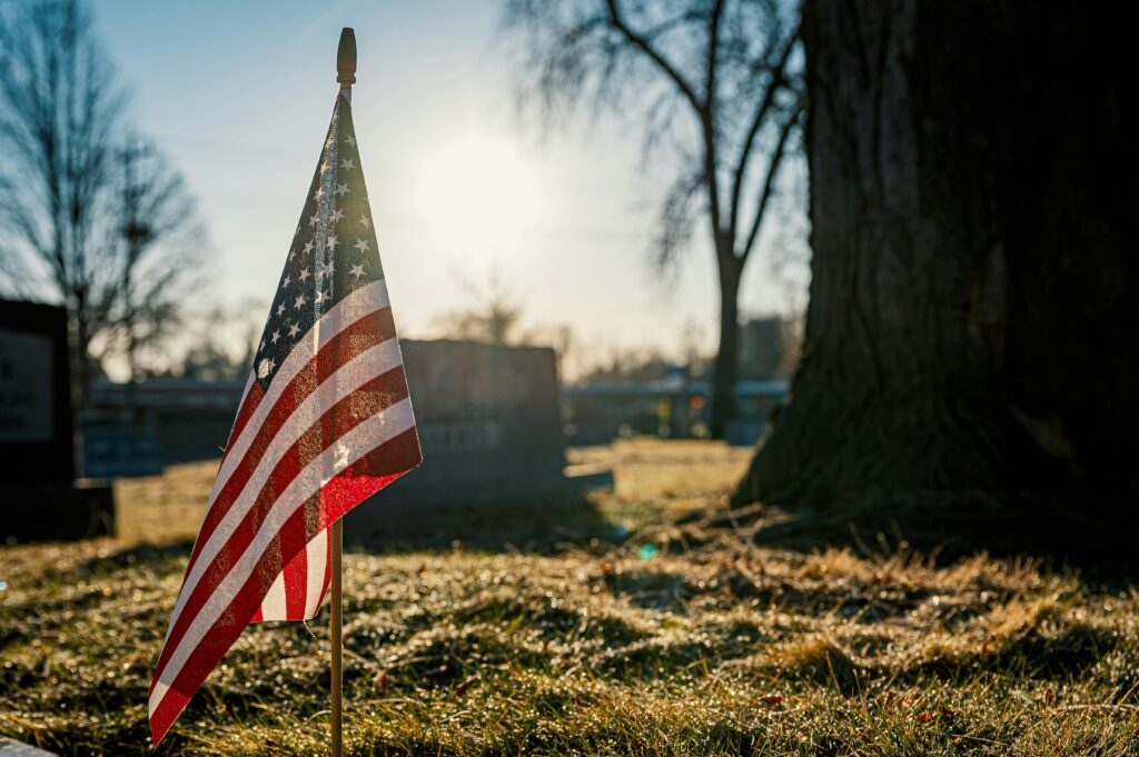 An American flag stands solemnly in a sunlit cemetery, symbolizing honor and remembrance.